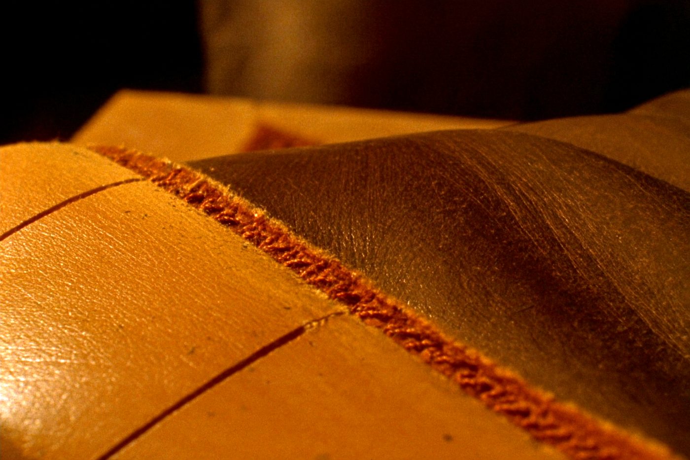 Close view of a heavy waxed thread seam running across two panels of tan leather.